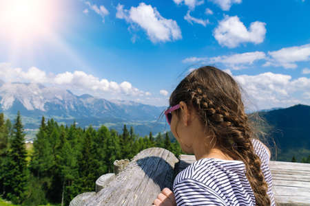Girl hiking on beautiful summer day in alps mountains Austria, resting on rock and admire amazing view to mountain peaks. Active family vacation leisure with kids.Outdoor fun and healthy activity.の写真素材