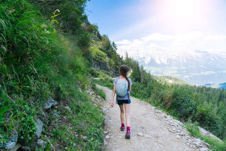 Girl hiking on beautiful summer day in alps mountains Austria, resting on rock and admire amazing view to mountain peaks. Active family vacation leisure with kids.Outdoor fun and healthy activity.の写真素材