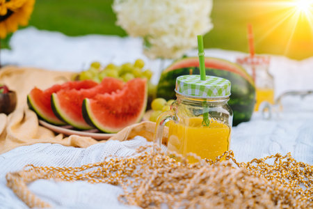 Summer picnic concept on sunny day with watermelon, fruit, bouquet hydrangea and sunflowers flowers. Picnic basket on grass with food and refreshing summer drink on knit blanket. Selective focusの写真素材
