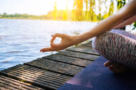young woman doing yoga asana in park. girl stretching exercise in yoga position. happy and healthy woman sitting in lotus position and practicing yoga. meditation and sport on sunset outdoors.の写真素材