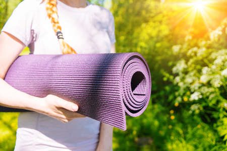 Sportswoman going to yoga practice with mat being ready for exercising in gym. Sporty Girl holding yoga mat and water bottle before fitness training. Concept of sports active lifestyle and health.の写真素材