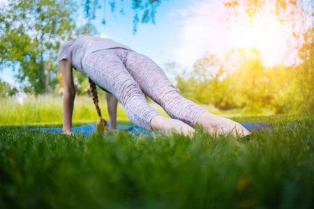 young woman doing yoga asana in park. girl stretching exercise in yoga position. happy and healthy woman sitting in lotus position and practicing yoga. meditation and sport on sunset outdoors.の写真素材