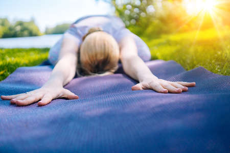 young woman doing yoga asana in park. girl stretching exercise in yoga position. happy and healthy woman sitting in lotus position and practicing yoga. meditation and sport on sunset outdoors.の写真素材
