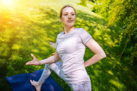 young woman doing yoga asana in park. girl stretching exercise in yoga position. happy and healthy woman sitting in lotus position and practicing yoga. meditation and sport on sunset outdoors.の写真素材