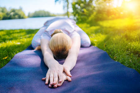 young woman doing yoga asana in park. girl stretching exercise in yoga position. happy and healthy woman sitting in lotus position and practicing yoga. meditation and sport on sunset outdoors.の写真素材