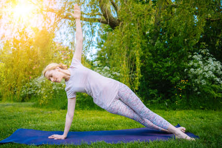 young woman doing yoga asana in park. girl stretching exercise in yoga position. happy and healthy woman sitting in lotus position and practicing yoga. meditation and sport on sunset outdoors.の写真素材