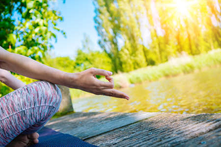 young woman doing yoga asana in park. girl stretching exercise in yoga position. happy and healthy woman sitting in lotus position and practicing yoga. meditation and sport on sunset outdoors.の写真素材