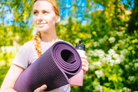 Sportswoman going to yoga practice with mat being ready for exercising in gym. Sporty Girl holding yoga mat and water bottle before fitness training. Concept of sports active lifestyle and health.の写真素材
