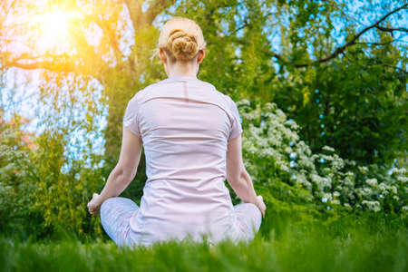 young woman doing yoga asana in park. girl stretching exercise in yoga position. happy and healthy woman sitting in lotus position and practicing yoga. meditation and sport on sunset outdoors.の写真素材