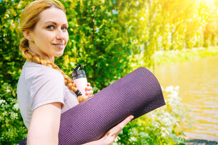 Sportswoman going to yoga practice with mat being ready for exercising in gym. Sporty Girl holding yoga mat and water bottle before fitness training. Concept of sports active lifestyle and health.の写真素材