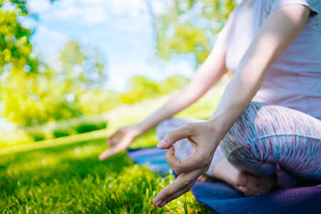 young woman doing yoga asana in park. girl stretching exercise in yoga position. happy and healthy woman sitting in lotus position and practicing yoga. meditation and sport on sunset outdoors.の写真素材