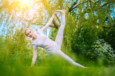 young woman doing yoga asana in park. girl stretching exercise in yoga position. happy and healthy woman sitting in lotus position and practicing yoga. meditation and sport on sunset outdoors.の写真素材