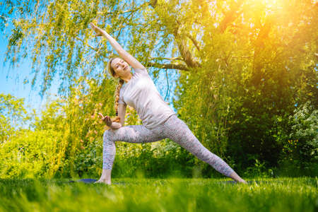 young woman doing yoga asana in park. girl stretching exercise in yoga position. happy and healthy woman sitting in lotus position and practicing yoga. meditation and sport on sunset outdoors.の写真素材