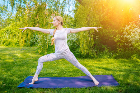 young woman doing yoga asana in park. girl stretching exercise in yoga position. happy and healthy woman sitting in lotus position and practicing yoga. meditation and sport on sunset outdoors.の写真素材