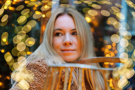 Girl walking in Christmas traditional market decorated with holiday lights in the evening. Winter portrait beautiful young woman outdoors in front of Xmas holidays decorations.の写真素材