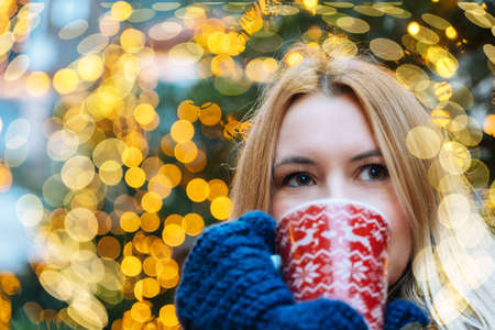 Girl walking in Christmas traditional market decorated with holiday lights in the evening. Winter portrait beautiful young woman outdoors in front of Xmas holidays decorations.の写真素材
