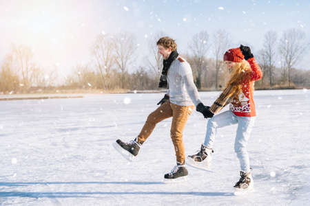 Loving couple in warm sweaters having fun on ice. Woman and man ice skating outdoors in sunny snowy day. Active date on ice arena in winter Christmas Eve. Romantic activities and lifestyle concept.の写真素材