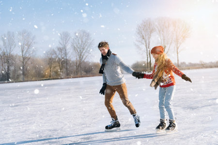 Loving couple in warm sweaters having fun on ice. Woman and man ice skating outdoors in sunny snowy day. Active date on ice arena in winter Christmas Eve. Romantic activities and lifestyle concept.の写真素材