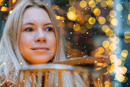 Girl walking in Christmas traditional market decorated with holiday lights in the evening. Winter portrait beautiful young woman outdoors in front of Xmas holidays decorations.の写真素材