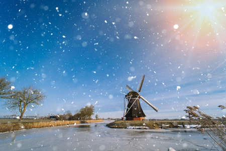 Typical winter dutch landscape with windmill. frozen canal in netherlands. Traditional winter holland scene. winter snow covering windmills and waterの写真素材