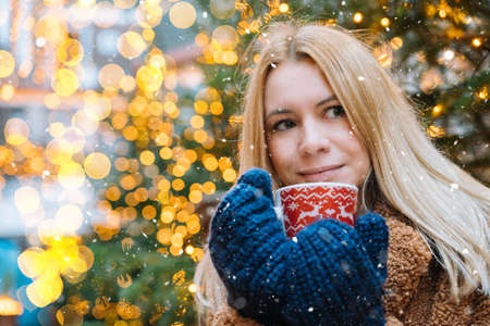 Girl walking in Christmas traditional market decorated with holiday lights in the evening. Winter portrait beautiful young woman outdoors in front of Xmas holidays decorations.の写真素材