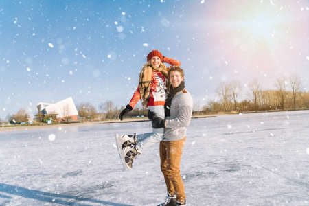 Loving couple in warm sweaters having fun on ice. Woman and man ice skating outdoors in sunny snowy day. Active date on ice arena in winter Christmas Eve. Romantic activities and lifestyle concept.の写真素材