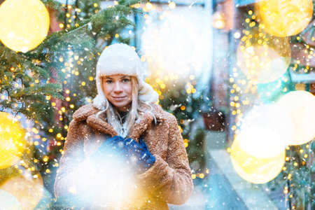 Girl walking in Christmas traditional market decorated with holiday lights in the evening. Winter portrait beautiful young woman outdoors in front of Xmas holidays decorations.の写真素材