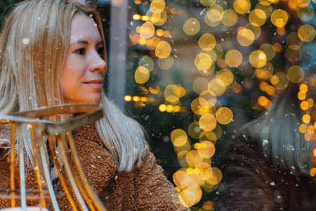 Girl walking in Christmas traditional market decorated with holiday lights in the evening. Winter portrait beautiful young woman outdoors in front of Xmas holidays decorations.の写真素材