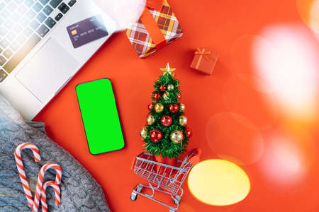 Christmas online shopping on laptop with credit card. New year decorations candy canes, shopping cart and presents box top view flat lay on red background. Merry Xmas winter holidays sales conceptの写真素材