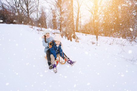 Two children ride on wooden retro sled on sunny winter day. Active winter outdoors games. Winter activities for kids. Children playing with snow in park.の写真素材