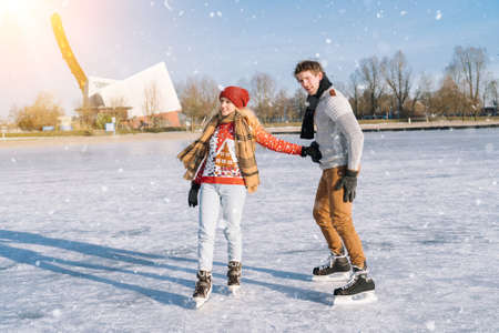 Loving couple in warm sweaters having fun on ice. Woman and man ice skating outdoors in sunny snowy day. Active date on ice arena in winter Christmas Eve. Romantic activities and lifestyle concept.の写真素材