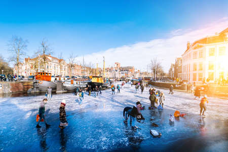 People ice scating on frozen canal in city center in Netherlands. Peoples making pictures, walking and skating on frozen canal in winter. Winter fun in cityGroningen. Netherlands. 14.02.2021.のeditorial素材