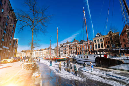 People ice scating on frozen canal in city center in Netherlands. Peoples making pictures, walking and skating on frozen canal in winter. Winter fun in cityGroningen. Netherlands. 14.02.2021.のeditorial素材