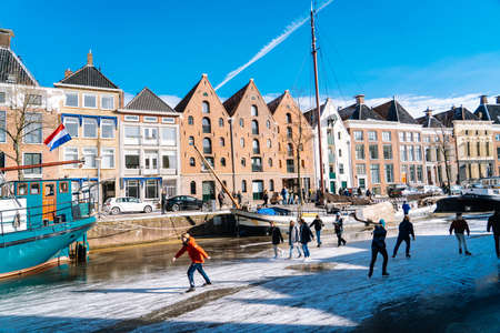 People ice skating on frozen canal in city center in Netherlands. Peoples making pictures, walking and skating on frozen canal in winter. Winter fun in cityGroningen. Netherlands. 14.02.2021.のeditorial素材