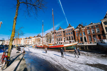 People ice skating on frozen canal in city center in Netherlands. Peoples making pictures, walking and skating on frozen canal in winter. Winter fun in cityGroningen. Netherlands. 14.02.2021.のeditorial素材