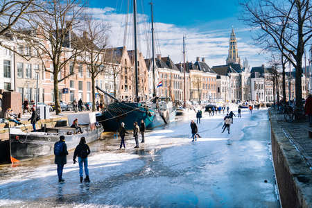 People ice skating on frozen canal in city center in Netherlands. Peoples making pictures, walking and skating on frozen canal in winter. Winter fun in cityGroningen. Netherlands. 14.02.2021.のeditorial素材