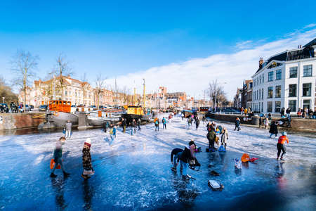 People ice skating on frozen canal in city center in Netherlands. Peoples making pictures, walking and skating on frozen canal in winter. Winter fun in cityGroningen. Netherlands. 14.02.2021.のeditorial素材