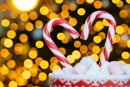 Christmas postcard with gingerbread cookie, red mug with christmas ornament on light bokeh from Xmas tree and red striped holidays candies. Xmas candies and cup with marshmallow on background.の写真素材
