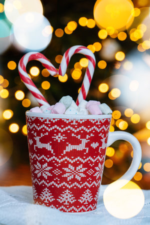 Christmas postcard with gingerbread cookie, red mug with christmas ornament on light bokeh from Xmas tree and red striped holidays candies. Xmas candies and cup with marshmallow on background.の写真素材