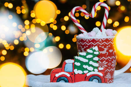Christmas postcard with gingerbread cookie, red mug with christmas ornament on light bokeh from Xmas tree and red striped holidays candies. Xmas candies and cup with marshmallow on background.の写真素材