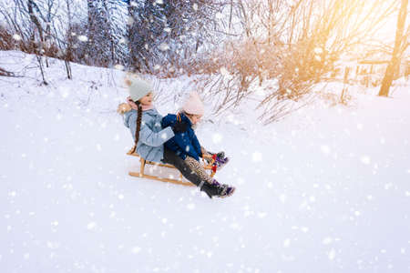 Two children ride on wooden retro sled on sunny winter day. Active winter outdoors games. Winter activities for kids. Children playing with snow in park.の写真素材