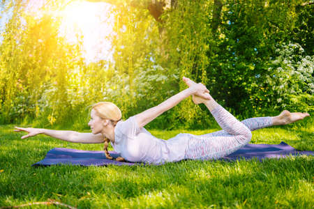 young woman doing yoga asana in park. girl stretching exercise in yoga position. happy and healthy woman sitting in lotus position and practicing yoga. meditation and sport on sunset outdoors.の写真素材