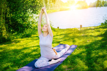 young woman doing yoga asana in park. girl stretching exercise in yoga position. happy and healthy woman sitting in lotus position and practicing yoga. meditation and sport on sunset outdoors.の写真素材