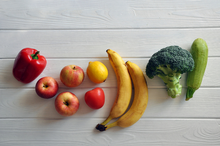 Top-view of bright fresh apples, banana, pepper, lemon, tomato, broccoli and zucchini on the white wooden backgroundの写真素材