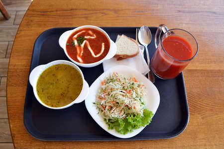 Ukrainian borsh, solyanka, cabbage salad with fresh tomato juice and bread, simple traditional lunch on the wooden table in a local canteen, top viewの写真素材