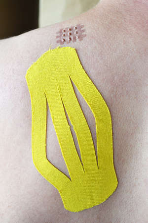 Big yellow medical taping and little cross medical taping on the Caucasian man's shoulder blade, selective focusの写真素材