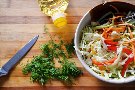 Cooking a vegetable salad in a ceramic bowl - with cabbage, pepper, carrot, dill and olive oil....