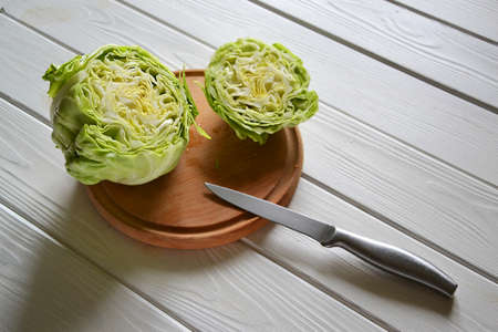 Fresh raw chopped cabbage on the wooden plate with knife on the white table, selective focusの写真素材
