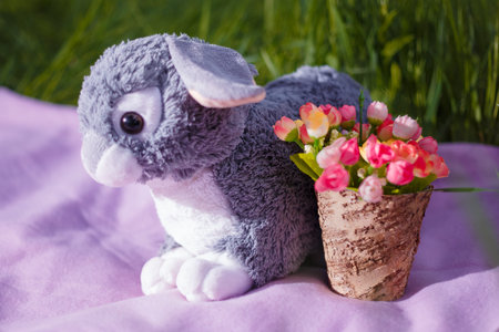 Easter decorative elements, vase with artificial flowers, plaid and bunny toy on green grass background.の写真素材