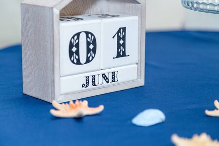 Cubic white wooden calendar with date 1 June standing on blue table cloth with some sea shells. Sea thematic party. Beginning of summer concept.の写真素材